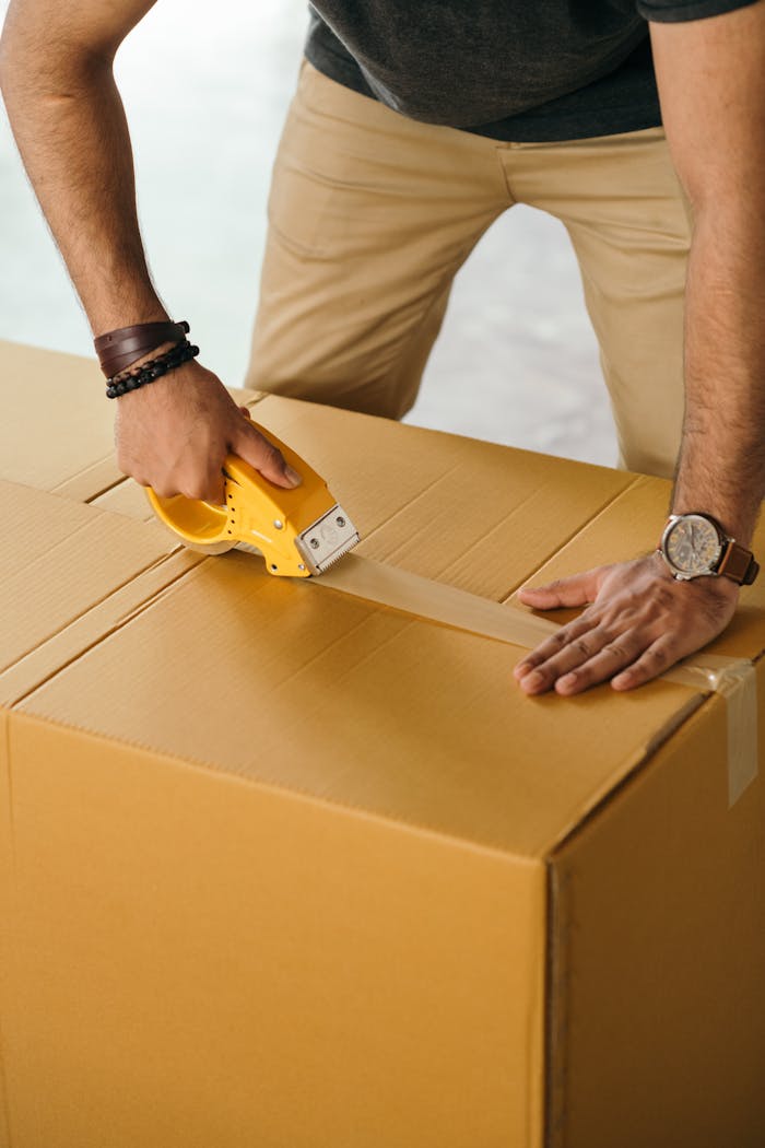services-01 Unrecognizable man sealing box with duck tape while preparing for moving out